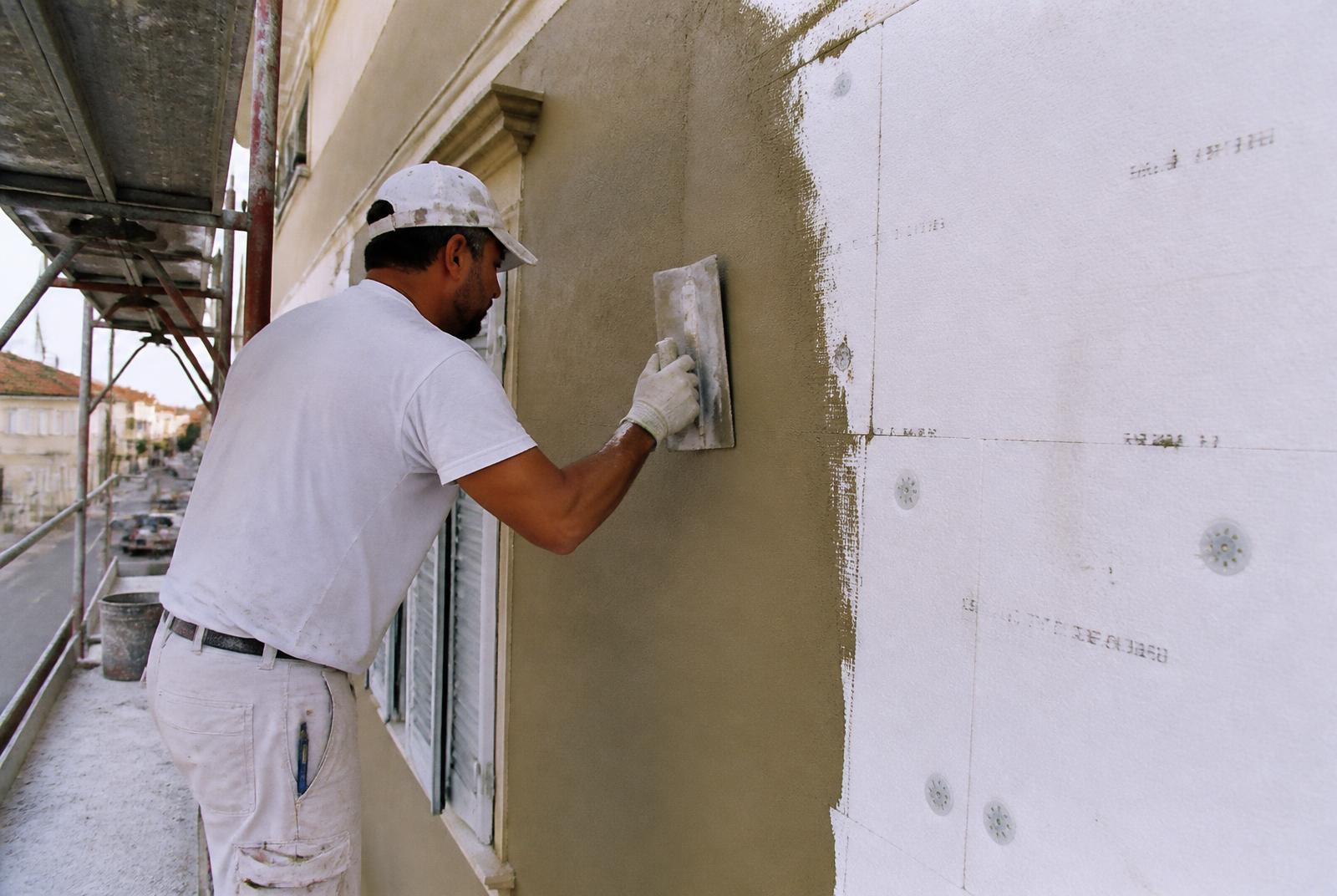 Operaio che rasa la facciata di un edificio con cappotto termico