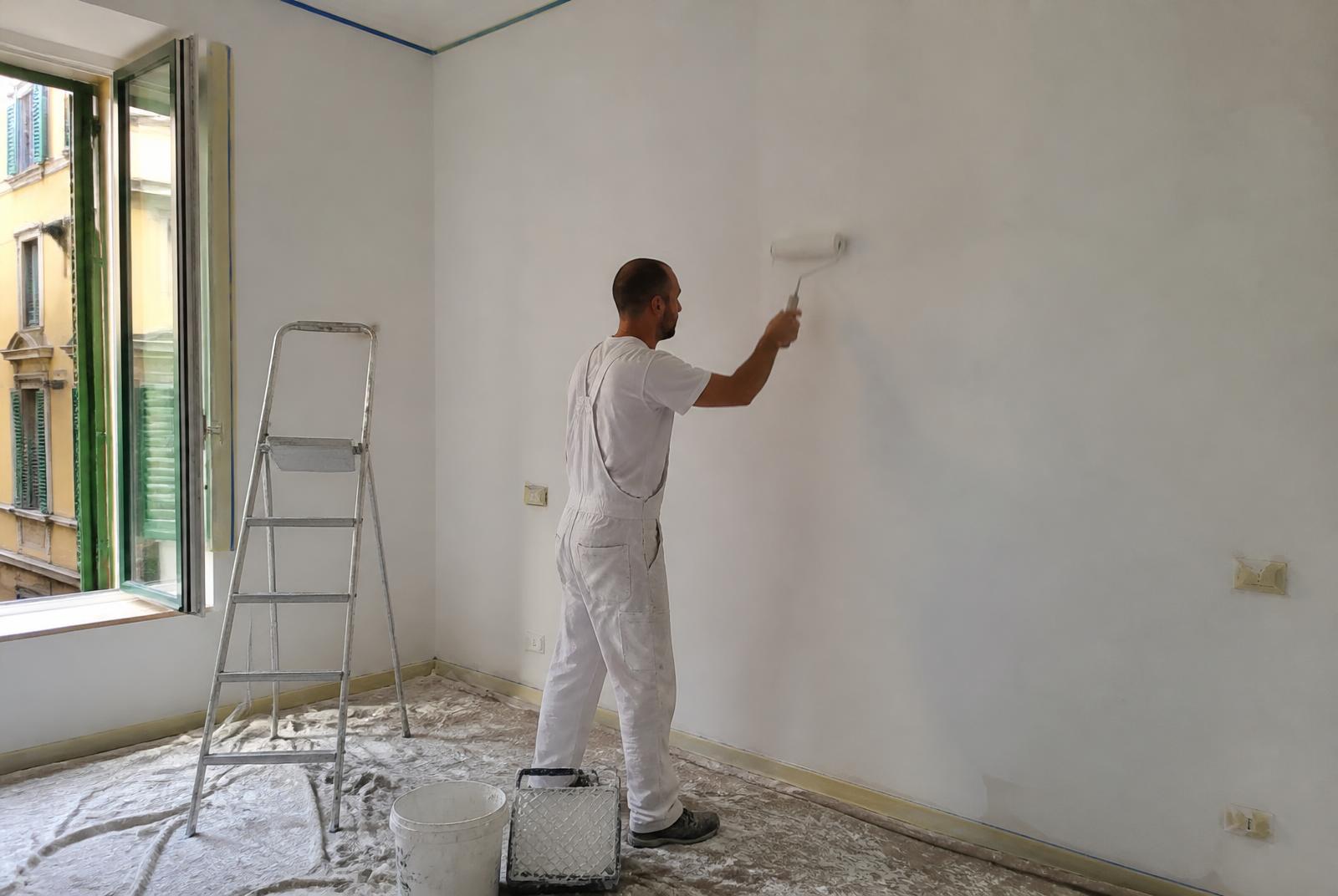 Imbianchino al lavoro con rullo su una parete di un appartamento